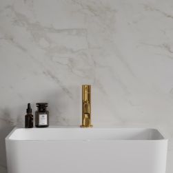 Widok od przodu na białą umywalkę ze złotą baterią stojącą Omnires Y na tle białej, marmurkowej ściany z szarymi żyłami