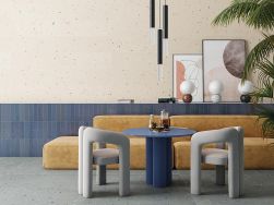 Pokój z podłogą wyłożoną niebieskimi płytkami lastryko Croccante-R Arandano z żółtą kanapą, niebieskim stolikiem, dwoma krzesełkami, obrazami i lampą wiszącą