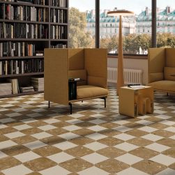 Salon wyłożony brązowymi i beżowymi płytkami imitującymi kamień z kolekcji Black&Cream z dwoma brązowymi fotelami, lampą stojącą i regałem z książkami