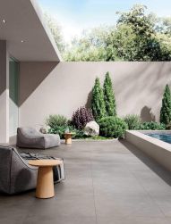 Taras wyłożony szarymi płytkami imitującymi beton All Around Concrete Grey, z dwoma fotelami, okrągłymi stolikami i roślinami
