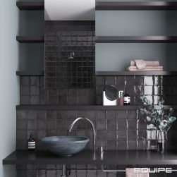 Nowoczesna, ciemna łazienka ze ścianą wyłożoną czarnymi cegiełkami z kolekcji Altea, z czarną półką wiszącą z umywalką nablatową i baterią stojącą, półkami i prostokątnym lustrem