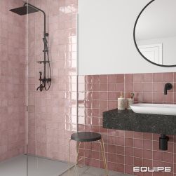 Łazienka ze ścianami wyłożonymi różowymi cegiełkami z kolekcji Altea z dużą kabiną prysznicową i grafitowym zestawem prysznicowym z deszczownicą, ciemną półką wiszącą z białą umywalką i baterią podtynkową, okrągłym lustrem i taboretem