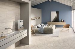 Sypialnia na poddaszu połączona z łazienką, wyłożona jasnymi płytkami drewnopodobnymi z kolekcji Alter Incontro Sbiancato, z podwójnym łóżkiem, szafką z lustrem, krzesłem i wiszącą szafką z umywalką