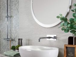 Fragment łazienki z białą umywalką nablatową, baterią podtynkową, okrągłym lustrem, kwiatem, zestawem prysznicowym i ścianą wyłożoną płytkami z kolekcji Emigres Dec Dorian Blanco