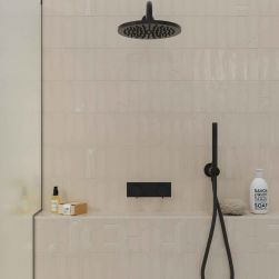 Ściana pod prysznicem wyłożoną beżowymi cegiełkami dekoracyjnymi w połysku Glow Decor Taupe Gloss z czarnym zestawem prysznicowym