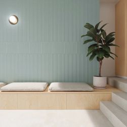 Pomieszczenie z miętowymi płytkami TP Med Celadon Green Matt na ścianie, z poduszkami do siedzenia i kwiatem w donicy