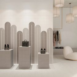 Nowoczesny, minimalistyczny sklep ze ścianą wyłożoną białymi cegiełkami matowymi T Dove Stone Matt, ze stojakami z butami i torebką, ubraniami na wieszakach i lampami wiszącymi