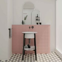 Łazienka z fragmentem ściany wyłożonym różowymi płytkami trójwymiarowymi Sweet Bars Blush Matt z umywalką stojącą na czarnym stelażu i dwoma lustrami