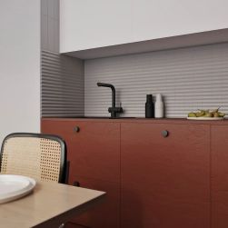 Ściana w kuchni wyłożona szarymi płytkami TP Up Grey Matt, z brązowymi meblami, białymi szafkami i stołem z krzesłem