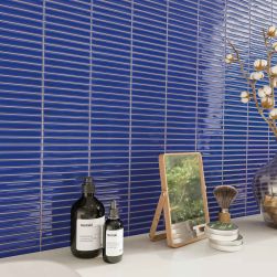 Ściana wyłożona intensywnie niebieskimi płytkami trójwymiarowymi Sweet Bars Indigo Gloss z białym blatem z lusterkiem i kosmetykami
