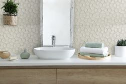 Widok w łazience na drewnianą szafkę z białym blatem, białą umywalką nablatową, podłużnym lustrem w ramie, akcesoriami i płytkami dekoracyjnymi z kolekcji Sutton