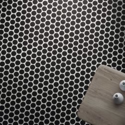 Widok z góry na podłogę wyłożoną czarną mozaiką z okrągłymi elementami Circle Black z drewnianym stolikiem i dwoma wazonami