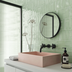 Zbliżenie na ścianę w łazience wyłożoną miętowymi cegiełkami dekoracyjnymi w połysku Glow Decor Mint Gloss z białą szafką z różową umywalka nablatową i okrągłym lustrem