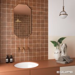 Fragment kolorowej łazienki z częścią ściany wyłożoną pomarańczowymi cegiełkami z kolekcji Argile, z pasują szafką w wpuszczaną umywalką i baterią podtynkową, lustrem w ramie, jasnymi wazonami, ręcznikiem i lampą wiszącą
