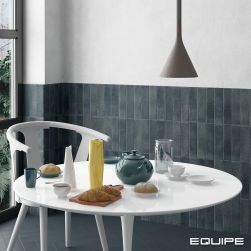Widok na biały, okrągły stolik zastawiony naczyniami i jedzeniem z białym krzesłem na tle ściany do połowy wyłożonej granatowymi cegiełkami z kolekcji Argile oraz z lampą wiszącą