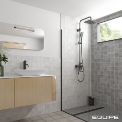 Jasna łazienka ze ścianami wyłożonymi białymi cegiełkami z kolekcji Argile, dużą kabiną prysznicową z oknem, jasną szafką drewnianą wiszącą z białą umyalką nablatową i grafitową baterią stojącą oraz lustrem