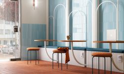 Restauracja ze ścianą wyłożoną błękitnymi cegiełkami w kształcie strzały z kolekcji Arrow Caribbean Blue, z ławą przy ścianie, okrągłymi stolikami i taboretami