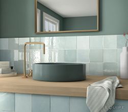 Turkusowo-zielona łazienka z drewnianym wiszącym blatem z zieloną umywalką nablatową i baterią stojącą złotą, lustrem w złotej ramie oraz cegiełkami ściennymi Artisan Aqua