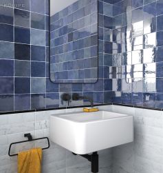 Fragment biało-niebieskiej łazienki z białą umywalką wiszącą, czarną baterią podtynkową, lustrem, żółtym ręcznikiem i płytkami Artisan Colonial Blue