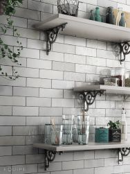 Zbliżenie na ścianę w kuchni wyłożoną białymi cegiełkami Artisan White z trzema białymi półkami wiszącymi z różnymi naczyniami i słoikami