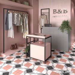 Pastelowo-różowy sklep odzieżowy wyłożony płytkami bazowymi i patchworkowymi z kolekcji Bauhome, z wieszakiem z ubraniami, stolikiem z akcesoriami, szarym biurkiem z komputerem i kwiatem