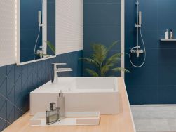 Łazienka z niebieskimi ścianami, jasnym, drewnianym blatem z białą umywalką nablatową i baterią umywalkową stojącą w chromie Deante Corio oraz lustrem i strefą prysznicową