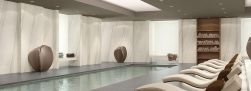 Pomieszczenie spa z basenem z płytkami imitującymi marmur Marmi Maxfine Bianco Lasa na ścianach, z leżakami