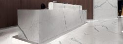 Pomieszczenie publiczne wyłożone płytkami imitującymi marmur Marmi Maxfine Bianco Venato Extra z dużym biurkiem