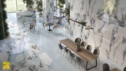 Duża, przestronna restauracja wyłożona płytkami imitującymi marmur z kolekcji Unique Marble Marmo Bianco Siena, z długimi stołami i okrągłymi stolikami, krzesłami, barem i lampami wiszącymi