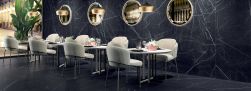 Restauracja wyłożona czarnymi płytkami imitującymi marmur Marmi Maxfine Black Marquinia, z okrągłymi stolikami i jasnymi krzesłami