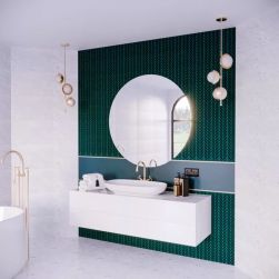 Biała łazienka z fragmentem ściany wyłożonym zieloną mozaiką w listki Bottany Capri z białą wanną, białą szafką wiszącą z umywalką nablatową, okrągłym lustrem i dwoma lampami wiszącymi