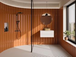 Półokrągła łazienka ze ścianami wyłożonymi brązowymi płytkami trójwymiarowymi Bow Brown z dużą strefą prysznicową, białą szafką wiszącą z umywalką nablatową, okrągłym lustrem i oknem
