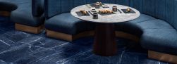 Podłoga w restauracji wyłożona niebieskimi płytkami imitującymi kamień Marmi Maxfine Brazilian Blue, z niebieską kanapą i okrągłym stołem z sushi