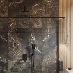 Widok na kabinę prysznicową wyłożoną brązowymi płytkami imitującymi kamień z baterią wannowo-prysznicową podtynkową czarną Omnires Baretti oraz zestawem prysznicowym czarnym