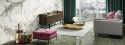Salon ze ścianą wyłożoną płytkami imitującymi marmur Marmi Maxfine Calacatta Grey, z szarą kanapą, różową pufą, okrągłym stolikiem i komodą