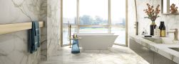 Elegancka łazienka wyłożona płytkami imitującymi marmur Marmi Maxfine Calacatta Oro, z wanną wolnostojącą przy oknie oraz wiszącą półką z dwiema umywalkami