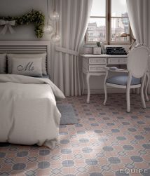 Romantyczna sypialnia z podwójnym łóżkiem, białym sekretarzykiem pod oknem z widokiem na miasto z krzesełkiem z błękitnym siedzeniem oraz płytkami podłogowymi z kolekcji Caprice