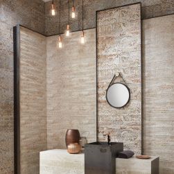 Fragment eleganckiej łazienki ze ścianami wyłożonymi dekoracyjnymi płytkami z kolekcji Carpet z kamienną półką z ciemną umywalką z ozdobami, okrągłym lustrem i lampą wiszącą