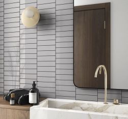 Fragment łazienki ze ścianą wyłożoną szarymi cegiełkami w połysku Costa Nova Grey Gloss z drewnianą szafką, marmurową umywalką i lustrem