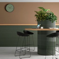 Restauracja z kolumną z roślinami wyłożoną zielonymi cegiełkami matowymi z reliefami Costa Nova Onda Laurel Green Matt z drewnianym blatem wok&oacute;ł niej oraz z taboretami