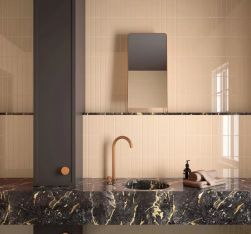 Ściana w łazience wyłożona morelowymi cegiełkami w połysku Costa Nova Straw Gloss z ciemnym, marmurowym blatem z umywalką, złotą baterią i małym lustrem
