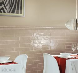 Fragment restauracji ze ścianą wyłożoną do połowy cegiełkami z listwą dekoracyjną z kolekcji Equipe Country ze stołami z czerwonymi obrusami i krzesłami oraz lampą wiszącą
