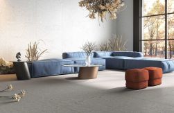 Duża niebieska kanapa, mały kawowy stolik, brązowe pufy, dekoracyjne rośliny, na podłodze płytki Cracked Graphite Natural Rect. 99,55x99,55 płytka imitująca beton