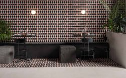 Restauracja, przy ścianie dwa czarne stoliki, krzesła, pod ściana długa kanapa, dekoracyjne rośliny, ściana i podłoga wyłożone Crea Como Natural 30,5x30,5 płytka dekoracyjna
