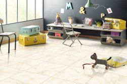Pokój dziecinny z podłogą wyłożoną beżowymi płytkami imitującymi kamień onyks w połysku Crown Onyx Light z niskim stołem z krzesłem, dwiema kolorowymi walizkami i zabawkami