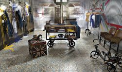 Sklep w stylu vintage z drewnianym stołem na kółkach na środku, z ubraniami, krzesłami, starym rowerem i płytkami podłogowymi FS-1 45x45