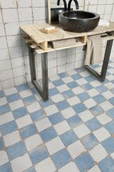 Fragment łazienki z jasnym drewnianym stołem, czarną umywalką nablatową, lustrem, beżowym ręcznikiem i płytkami podłogowymi FS Artisan Damero-A 33x33
