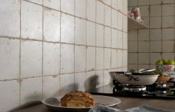 Fragment kuchni z naczyniami i jedzeniem oraz ścianą wyłożoną rustykalnymi płytkami FS Artisan-B 33x33