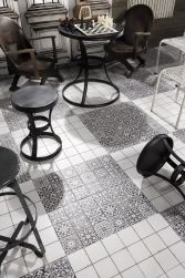 Zbliżenie na podłogę wyłożoną płytkami patchworkowymi FS Faenza-N 33x33 z czarnymi i białymi krzesełkami oraz stolikiem z szachami