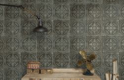 Zbliżenie na ścianę wyłożoną płytkami patchworkowymi reliefowymi FS Saja-N 33x33 z drewnianym stołem, kwiatem, czarną lampką